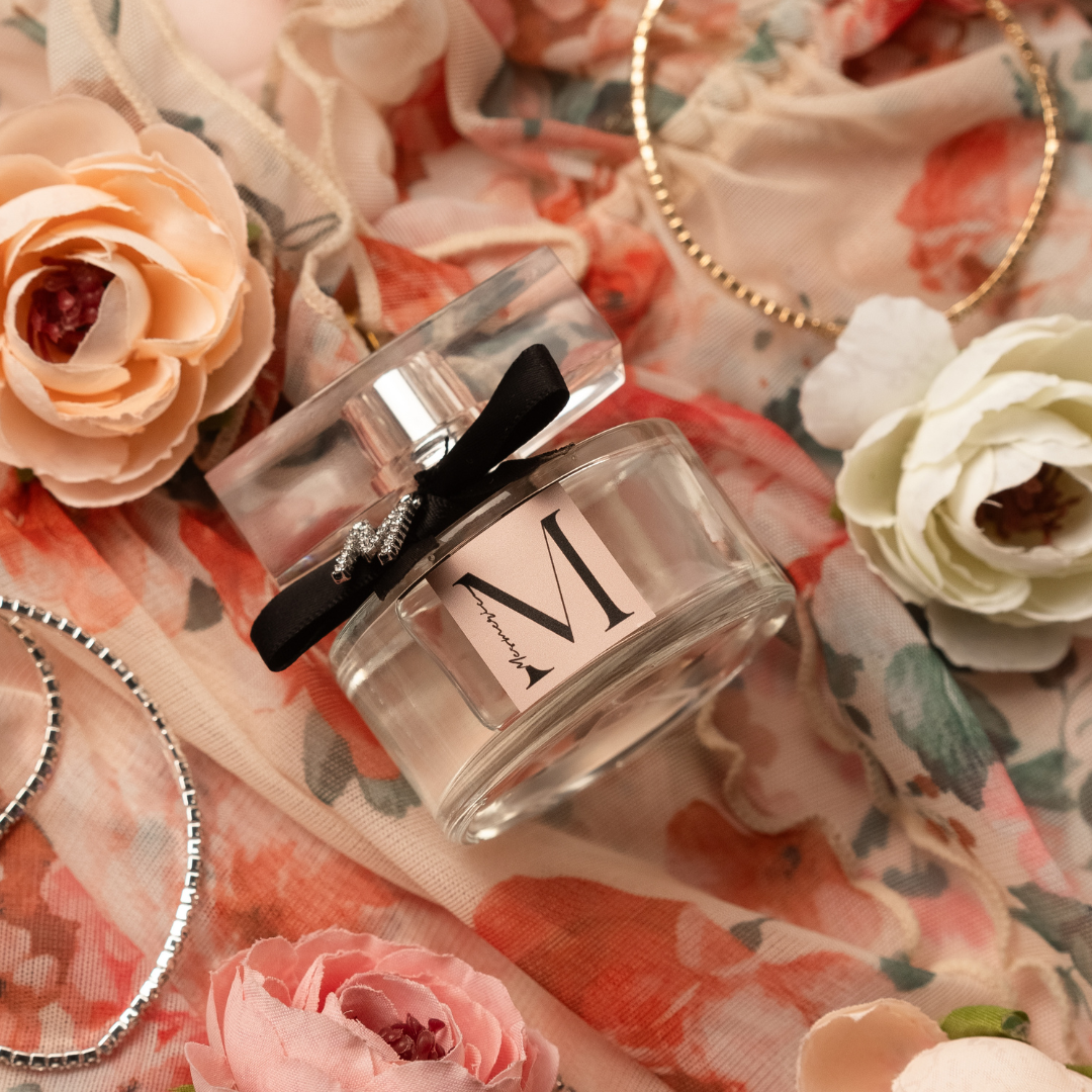 A bottle of M like Mesmeric parfume on flowered background with flowers and bracelets.