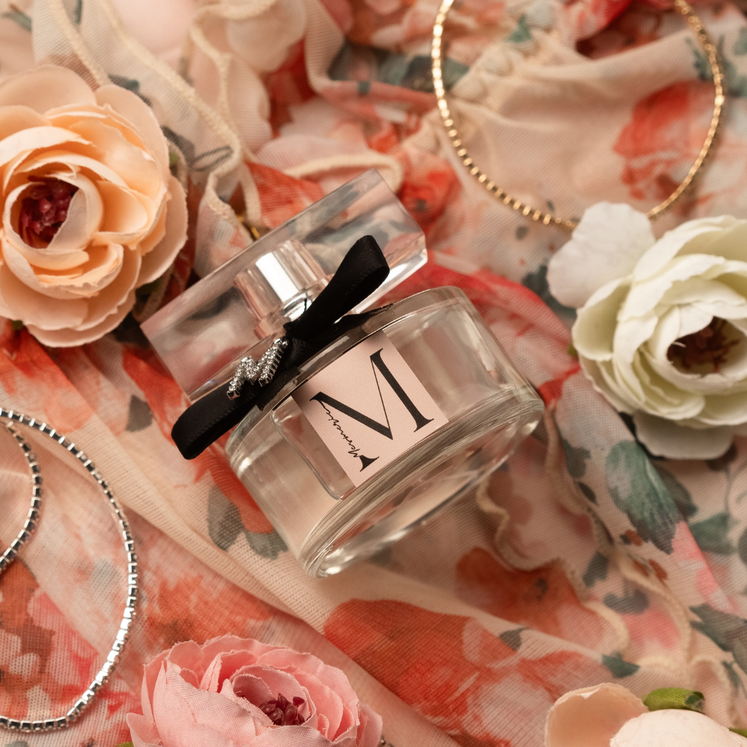 A bottle of M like Mesmeric parfume on flowered background with flowers and bracelets. 